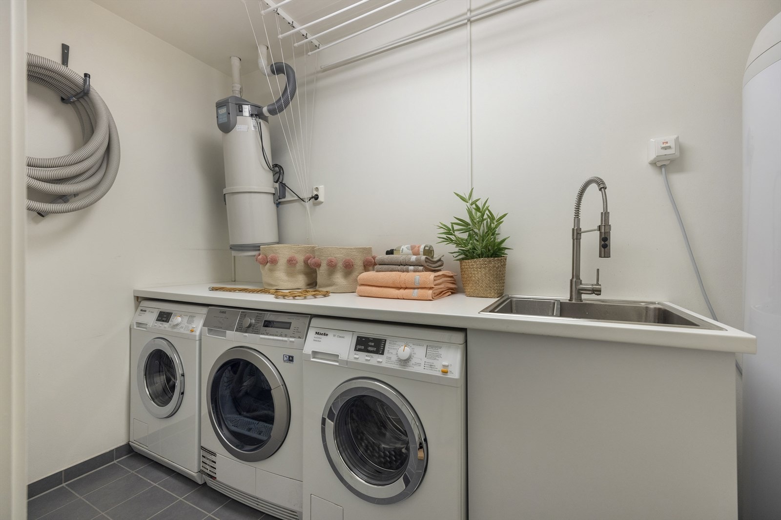 Praktisk vaskerom med støpt og flislagt gulv. Sentralstøvsuger. 2 x Miele vaskemaskin og AEG tørketrommel medfølger salget Galleribilde