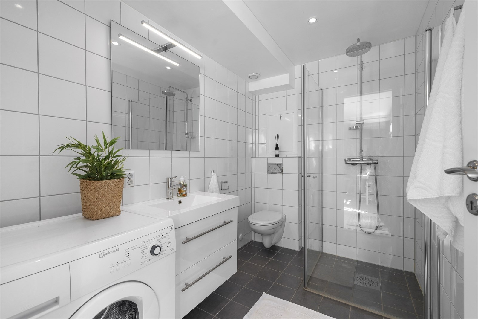 Dusjbad/wc i hybel. Badet har innredning med nedfelt servant, veggmontert toalett, dusjvegger/hjørne og opplegg for vaskemaskin Galleribilde