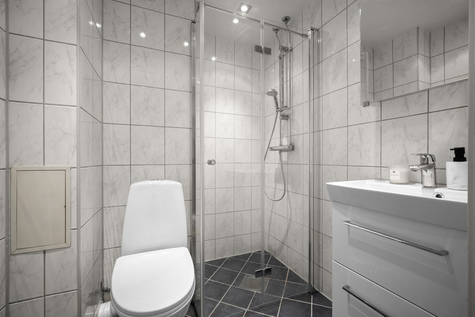 Delikat flislagt baderom med elektriske varmekabler i gulv fra 2009. Baderommet er pusset opp i borettslagets regi. Badet er utstyrt med toalett, vegghengte dusjdører i glass og servant på vegghengt servantskap. Spalte underkant dør for tilluft. Galleribilde