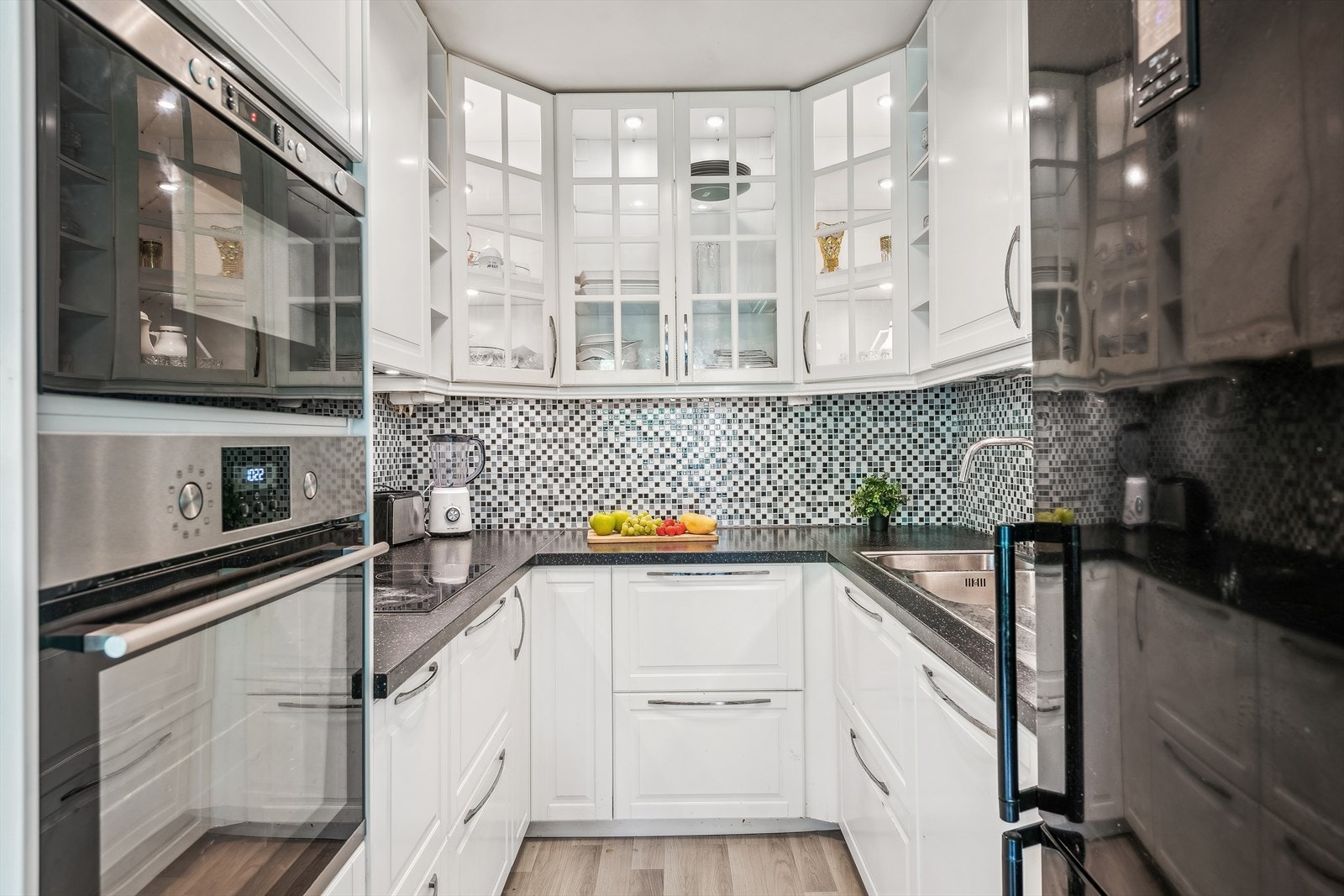 KJØKKEN | Kjøkkeninnredning med hvite profilerte fronter og med takhøye skap, enkelte overskap med fronter i glass, benkeplater i laminat, rustfri oppvaskkum med avrenningsplate, ventilator med kullfilter og integrerte hvitevarer. Fliser over benkeskap Galleribilde