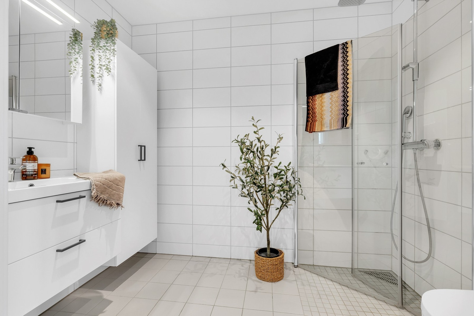 Lekkert bad med lyse fliser og varmekabler i gulv. Stor dusjnisje, vegghengt toalett og påkostet innredning. Galleribilde