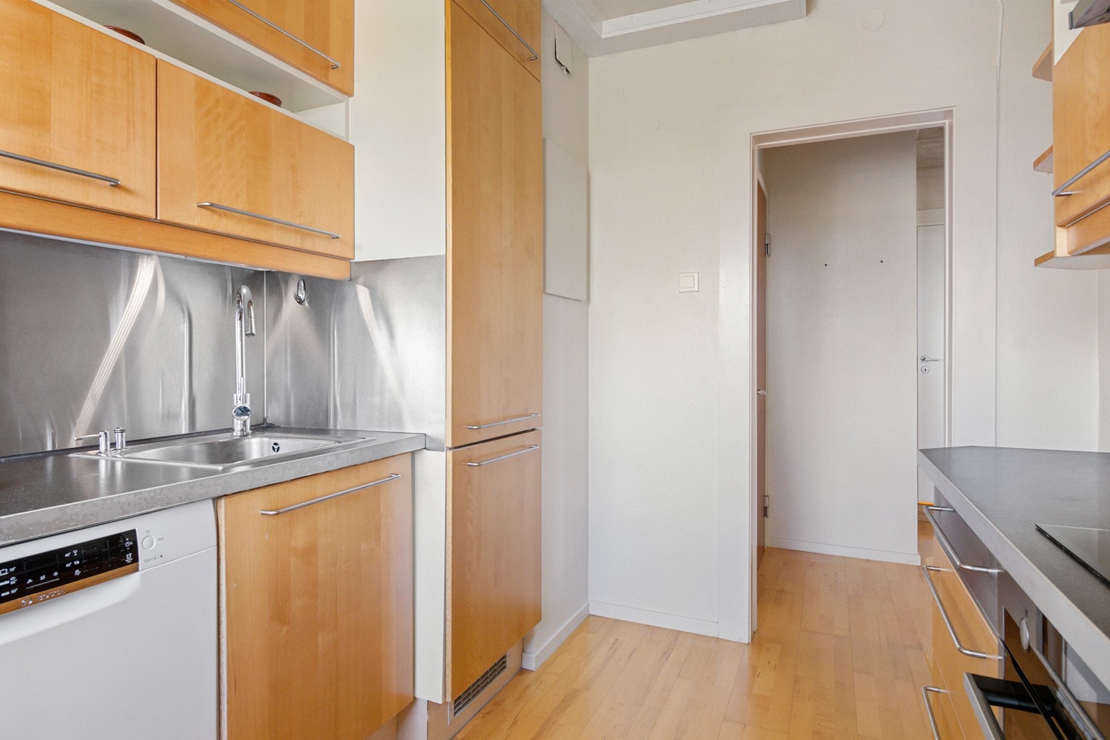 Ikea kjøkkeninnredning med glatte finerte skapfronter, laminat benkeplate med sprutplate på bakvegg, enkel oppvaskkum, ventilator og innfelte hvitevarer som koketopp, stekeovn, kjøl/- fryseskap, oppvaskmaskin. Galleribilde
