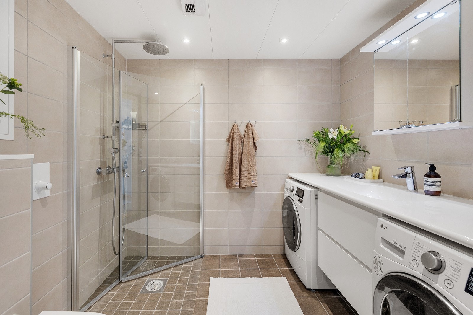 Lekkert bad med hvit moderne baderomsinnredning, vegghengt toalett og dusjnisje med dusjdører i herdet glass Galleribilde