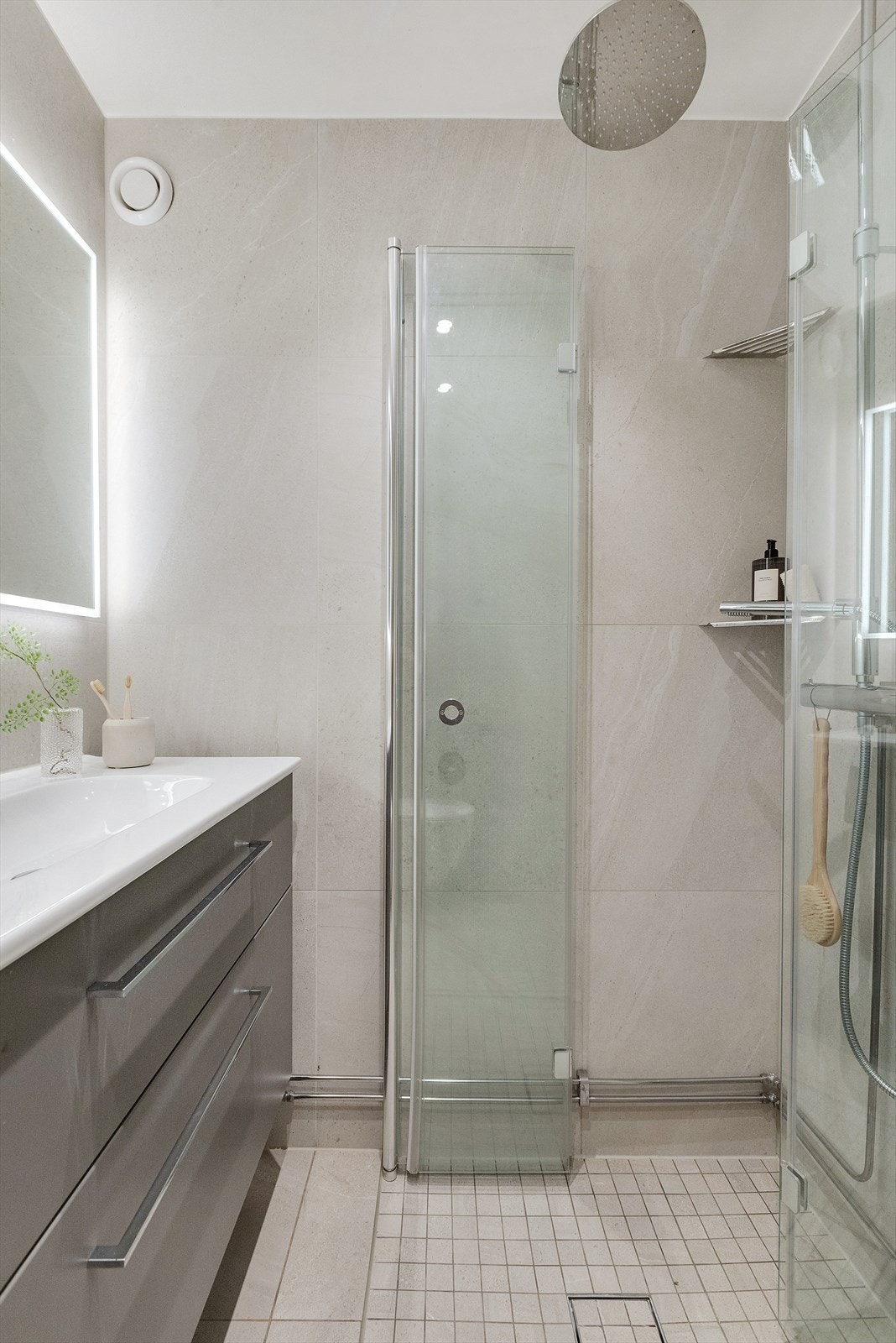 Badet er innredet med glatt baderomsinnredning med heldekkende servant nedfeldt i underskap, speil m/lys, veggmontert toalett og dusjhjørne m/glassdører. Galleribilde