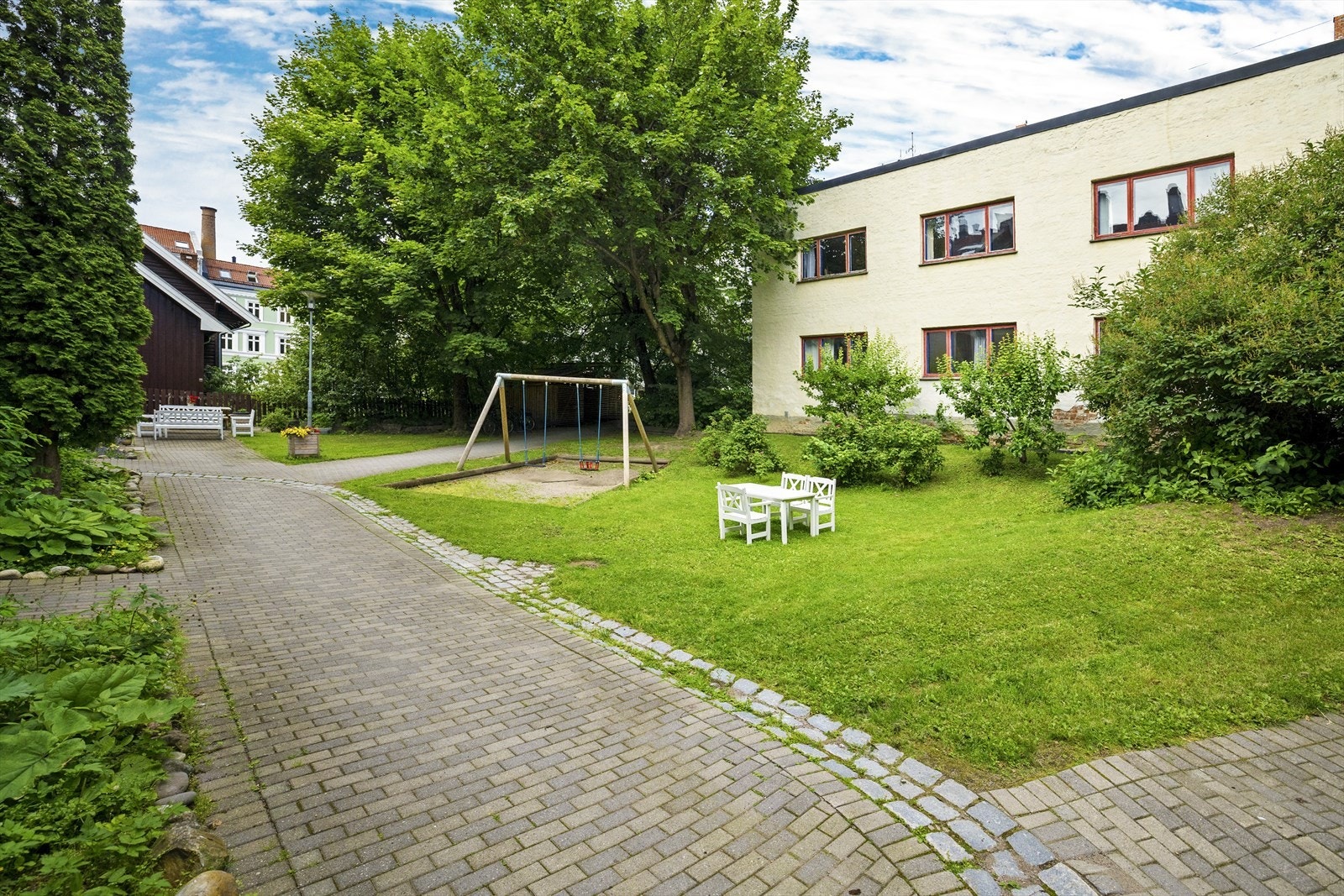 Pent opparbeidet bakgård med gressplen, beplantning, prydbusker, sittegruppe og lekeapparater. Galleribilde