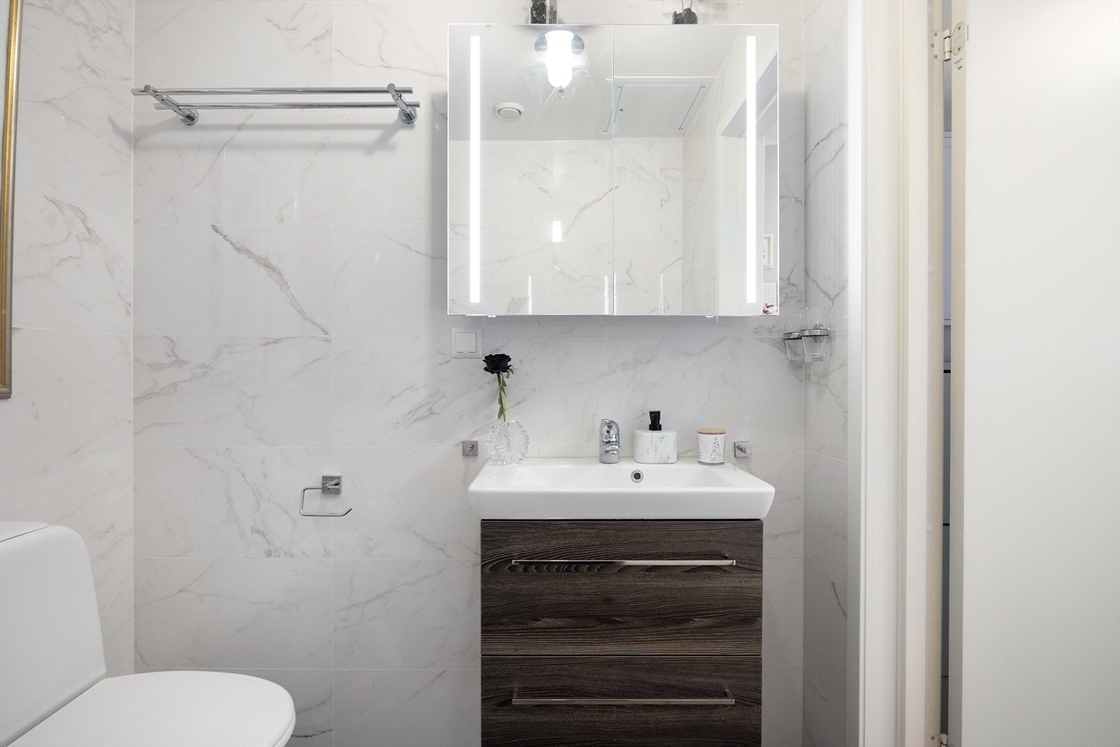 Badet består av servantskap med folierte fronter og heldekkende servant, speilskap med lysarmatur på vegg og gulvmontert klosett med utenpåliggende sisterne. Det er opplegg for vaskemaskin. Dusjhjørne med buede svingdører, sluk og blandebatteri. Galleribilde