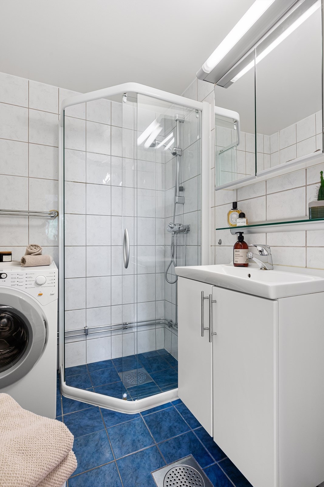 Dusjhjørne i glass, veggskap med profilert hvit skapfront og peilskap med belysning over servant Galleribilde