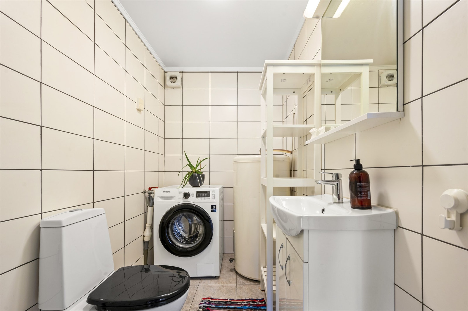 Badet er pent flislagt på gulv og vegger med varme i gulvet. Innredningen består blant annet av vegghengt servantskap med servant. Over servanten er det speil med lys. Galleribilde