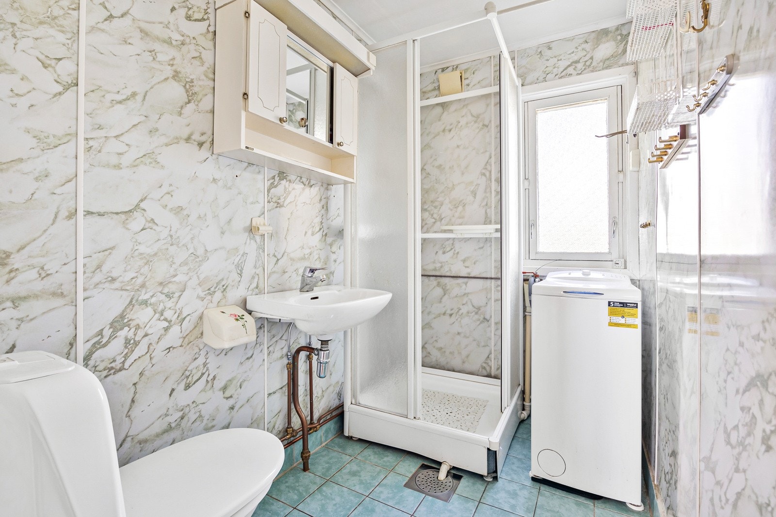 Bad fra byggår med våtromsplater på vegg og flislagt gulv med gulvvarme, dusjkabinett, gulvstående toalett og opplegg for vaskemaskin Galleribilde