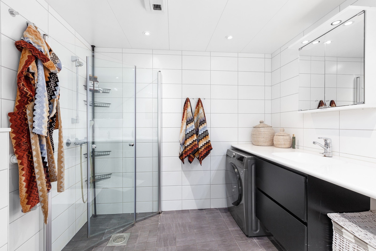 Lekkert og flislagt baderom med gulvvarme. Plass og opplegg til vaskemaskin og tørketrommel. Badet består av vegghengt toalett, benkeplate med innfelt servant og vegghengte dusjdører i glass. Galleribilde