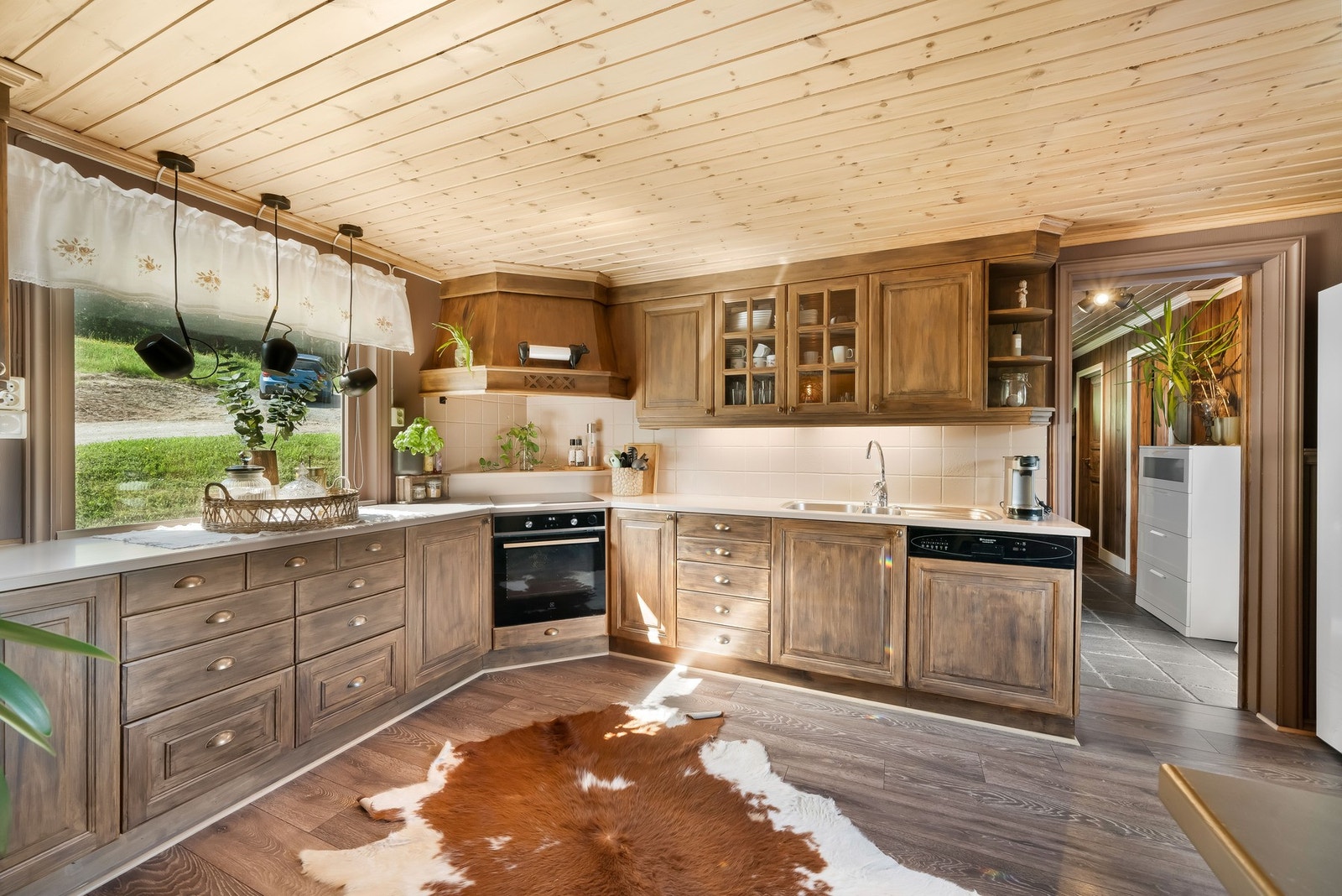 Kjøkken fra Øyfjell treindustri, fra omkring 2000. Gulv med laminat. Vegger med tapet og trepanel. Himling med trepanel. Innredning med heltre fronter. Heltre benkeplate med nedfelt dobbel kjøkkenkum og ett-greps blandebatteri. Integrert oppvaskmaskin, ko Galleribilde