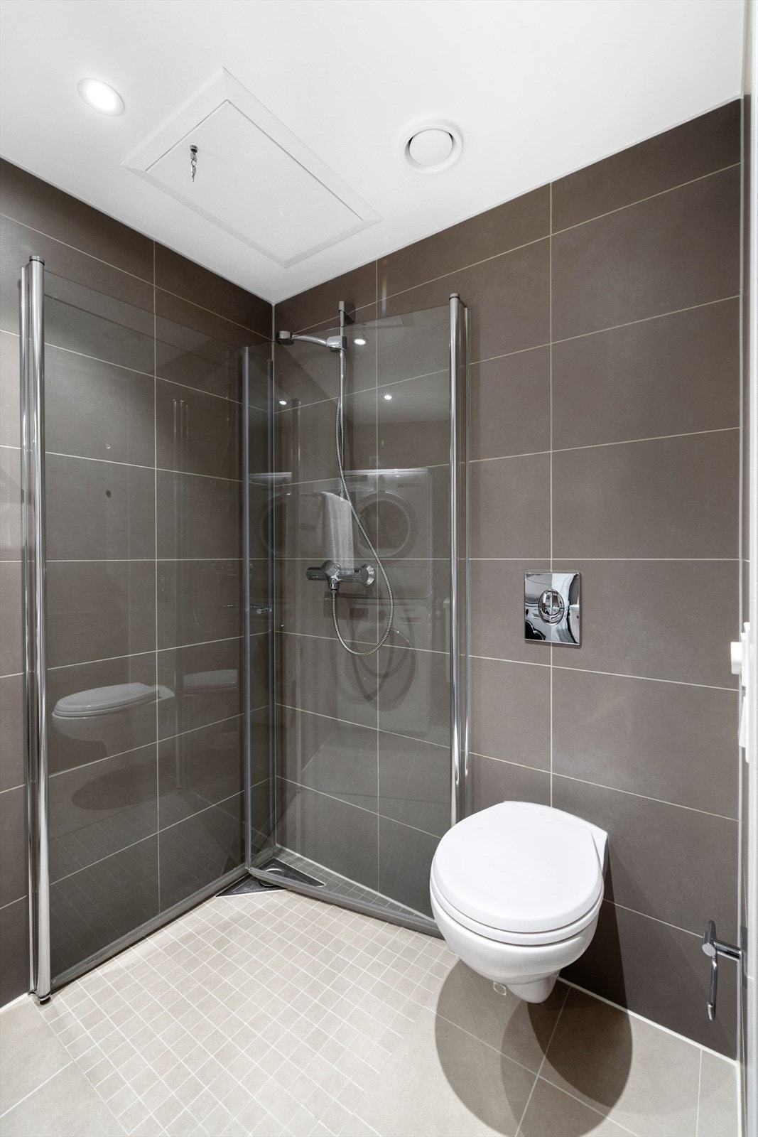 Badet er utstyrt med servantinnredning, speilskap, vegghengt toalett og dusjhjørne med innfellbare dusjdører. Galleribilde