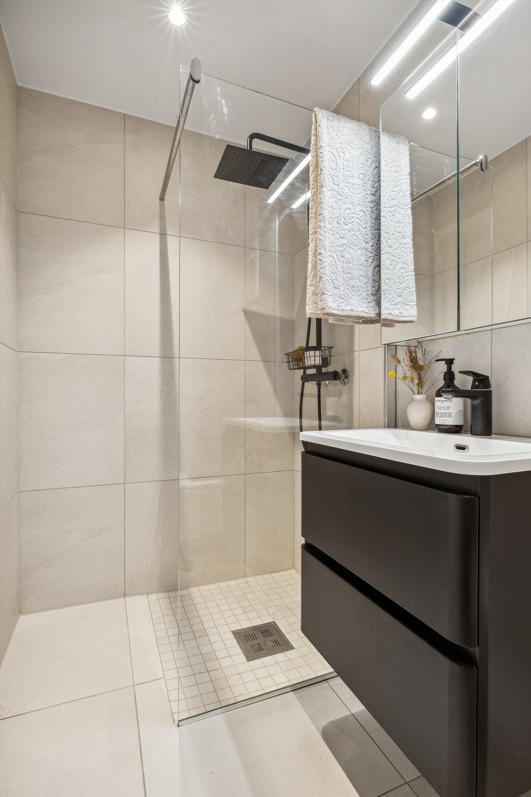 Flislagt baderom. Videre er badet innredet med servant, speilskap, vegghengt toalett og dusj med glassvegg. Det er uttak til vaskemaskin og elektriske varmekabler i gulv på badet. Galleribilde
