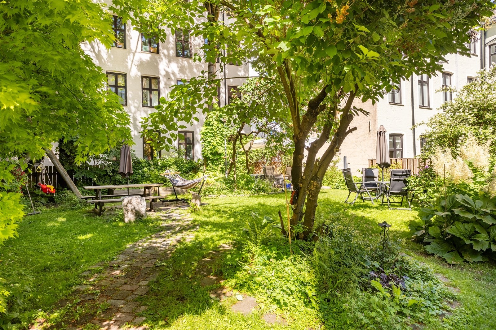 Bakgården er pent opparbeidet med beplantning og innredet med utemøbler som skaper et sosialt uteområde for beboerne. Galleribilde
