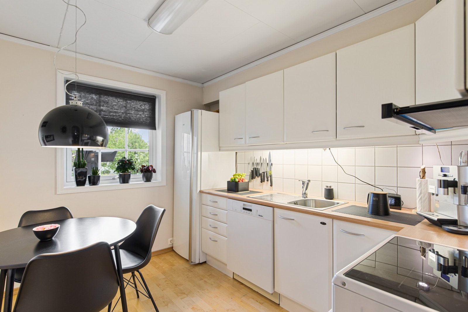 Kjøkkeninnredning med hvite, slette fronter, laminat benkeplate med flis mot overskap, ventilator og opplegg for oppvaskmaskin. Gode muligheter for spiseplass på kjøkkenet. Galleribilde