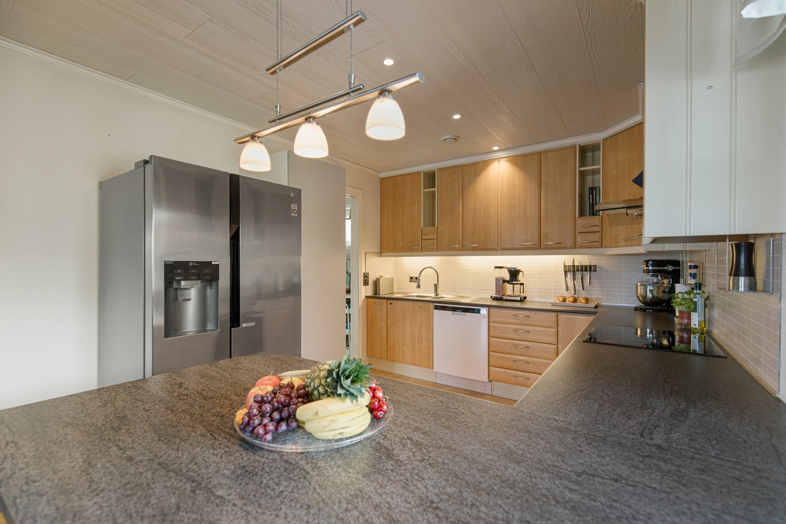 Stor og innholdsrik kjøkkeninnredning med slette fronter i bjørkefiner. Galleribilde