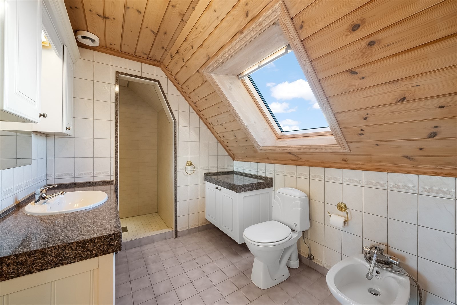 Bad med flis på gulv og vegg. Badet er innredet med baderomsinnredning, toalett, bidé og dusjnisje. Galleribilde