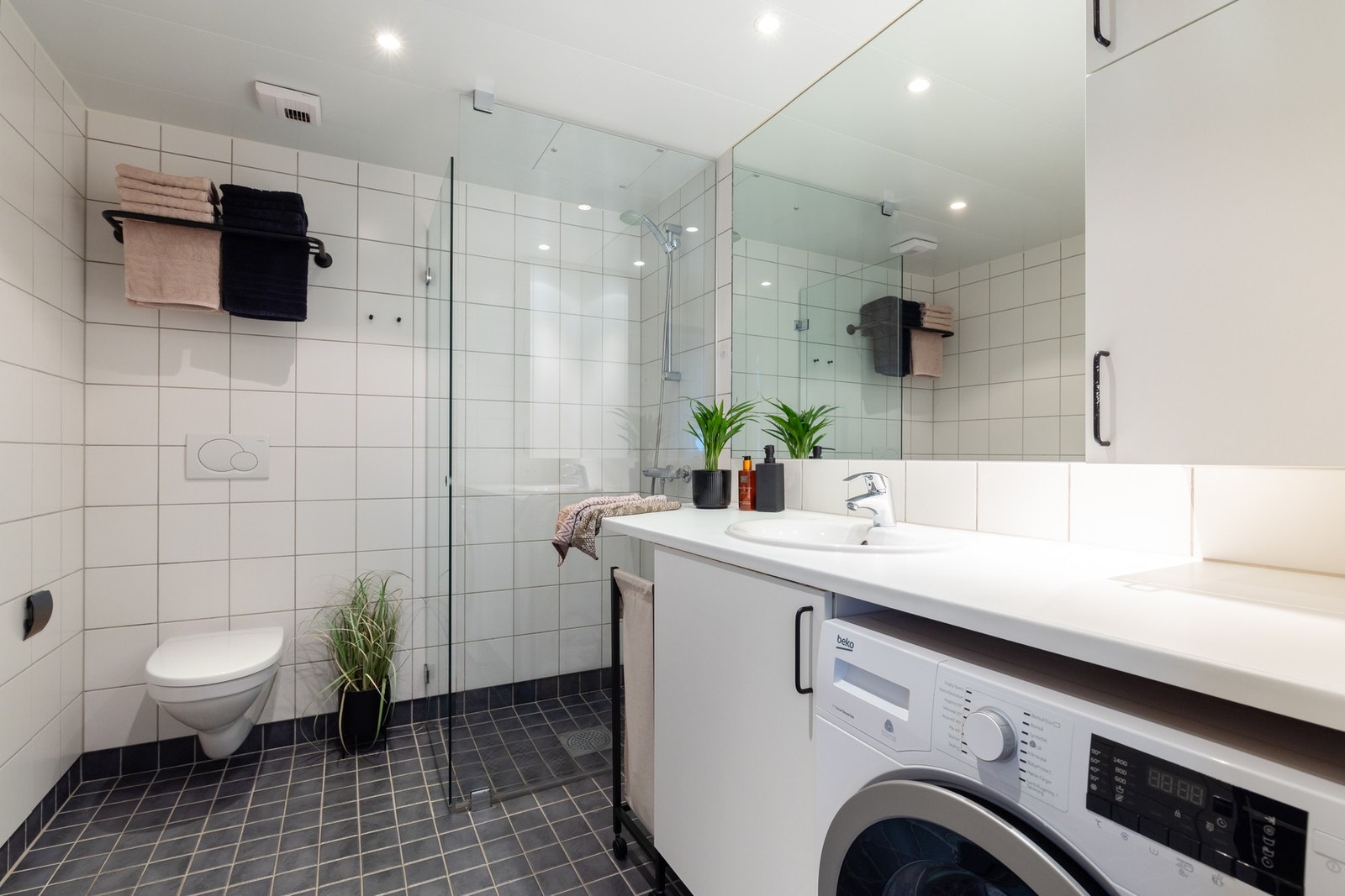 Boligens baderom er lyst og delikat, med varme i gulv og downlights i himling. Praktisk nisje for vaskemaskin under benk. Galleribilde