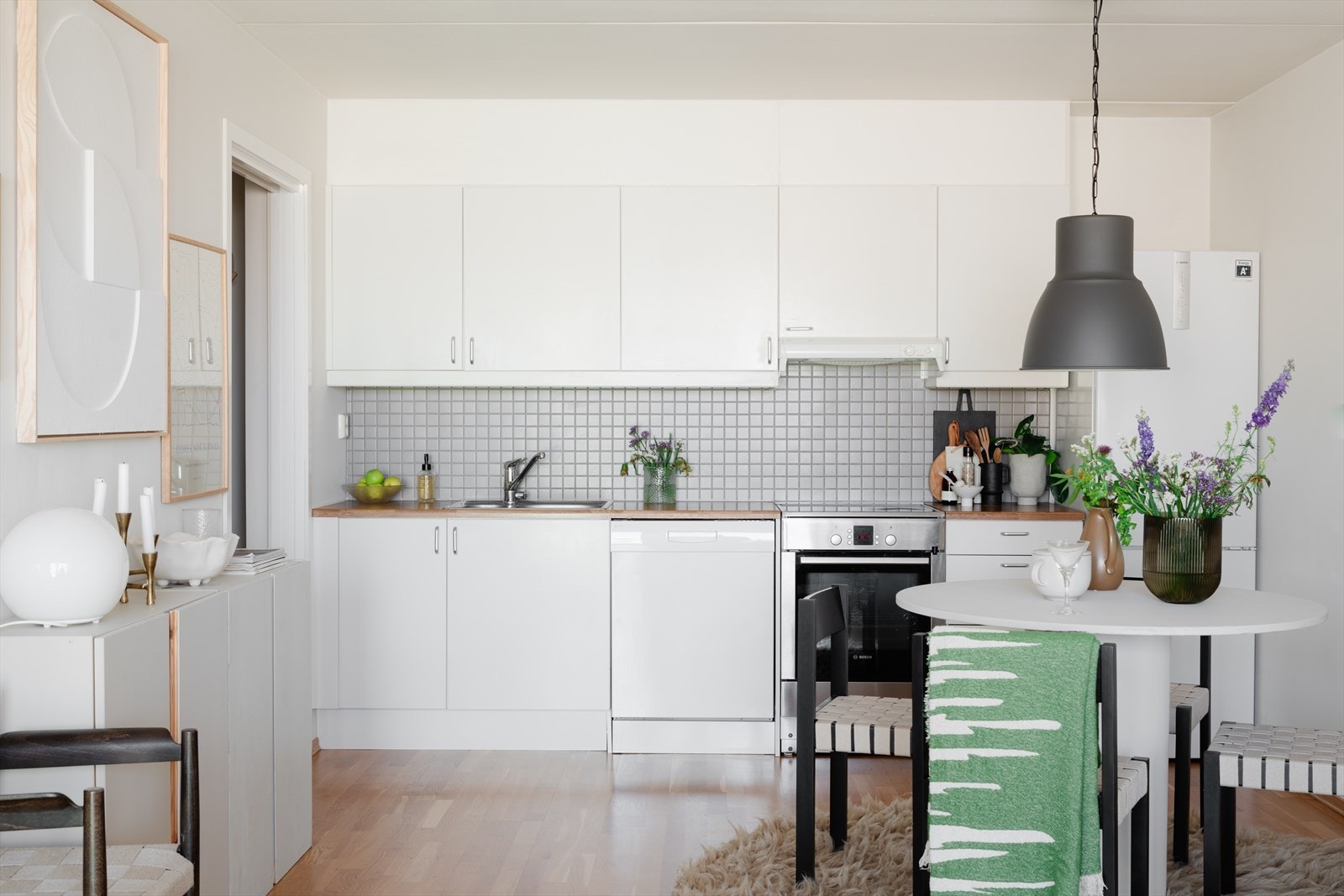 Kjøkkenet er lyst og tidløst med hvite matte fronter og laminat benkeplate med nedfelt kum i rustfritt stål. Ventilator koblet på mekanisk avtrekk over kokesone. Galleribilde