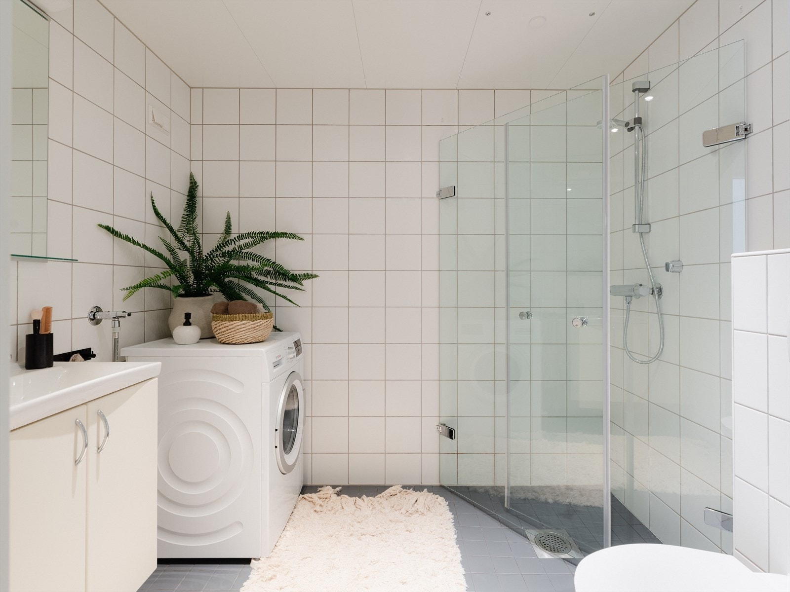 Badet er pent flislagt med hvite og grå fliser. Det er varme i gulvet og downlights i himlingen. Romslig dusjhjørne med svingbare dører i herdet glass (nye i 2015). Galleribilde