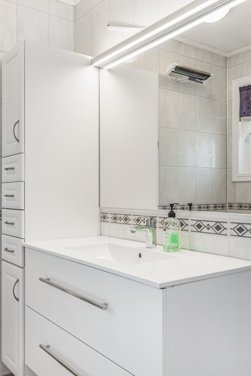 Det er montert badekar med armatur på vegg, toalett og reflektorovn. Det er en hvit baderomsinnredning med skuffer og heldekkende servant fra 2023, samt veggmontert høyskap, speil og belysning. Det er mekanisk ventilering i rommet. Galleribilde