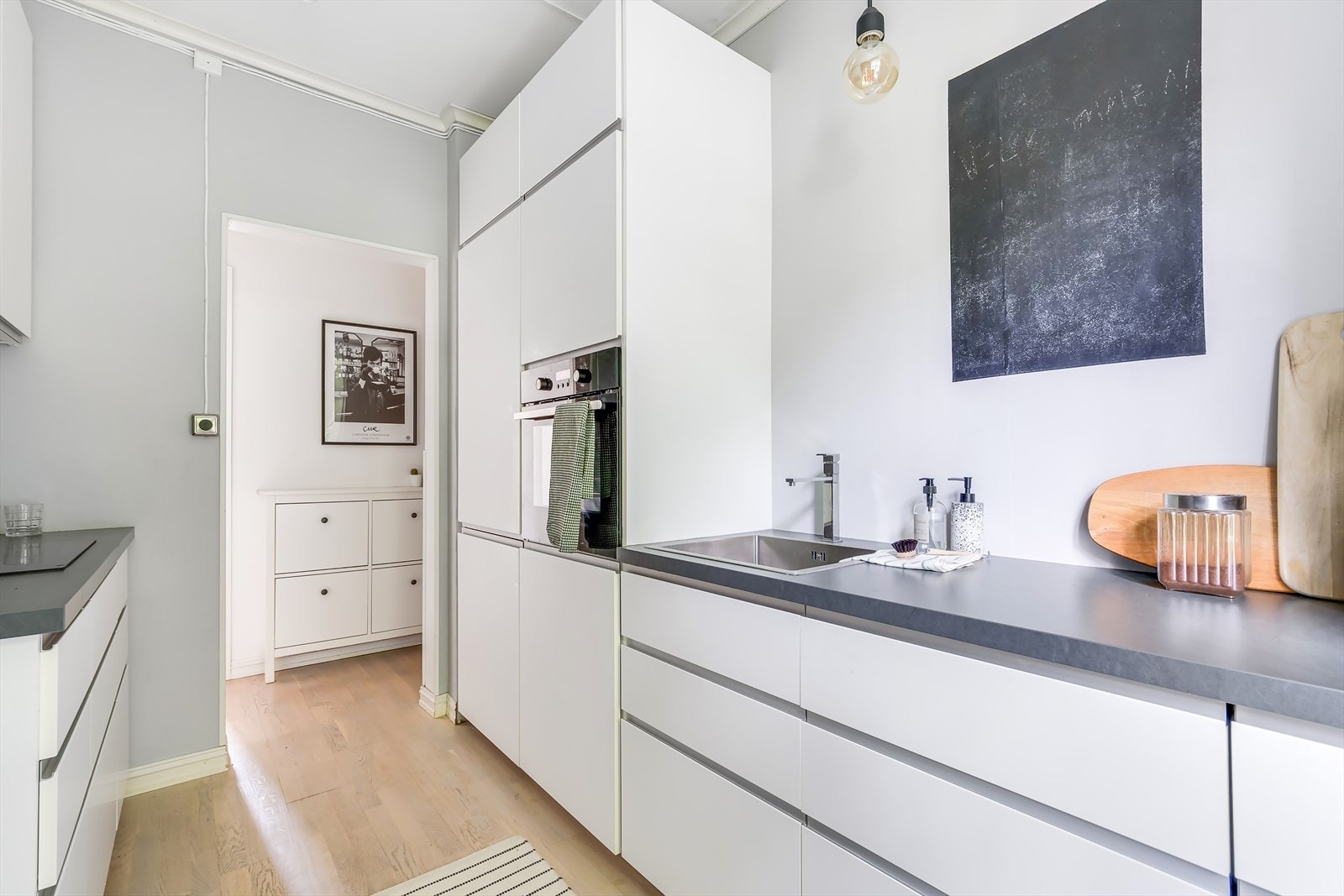 Hvit, stilren kjøkkeninnredning med benkeplate av laminat og integrerte hvitevarer Galleribilde