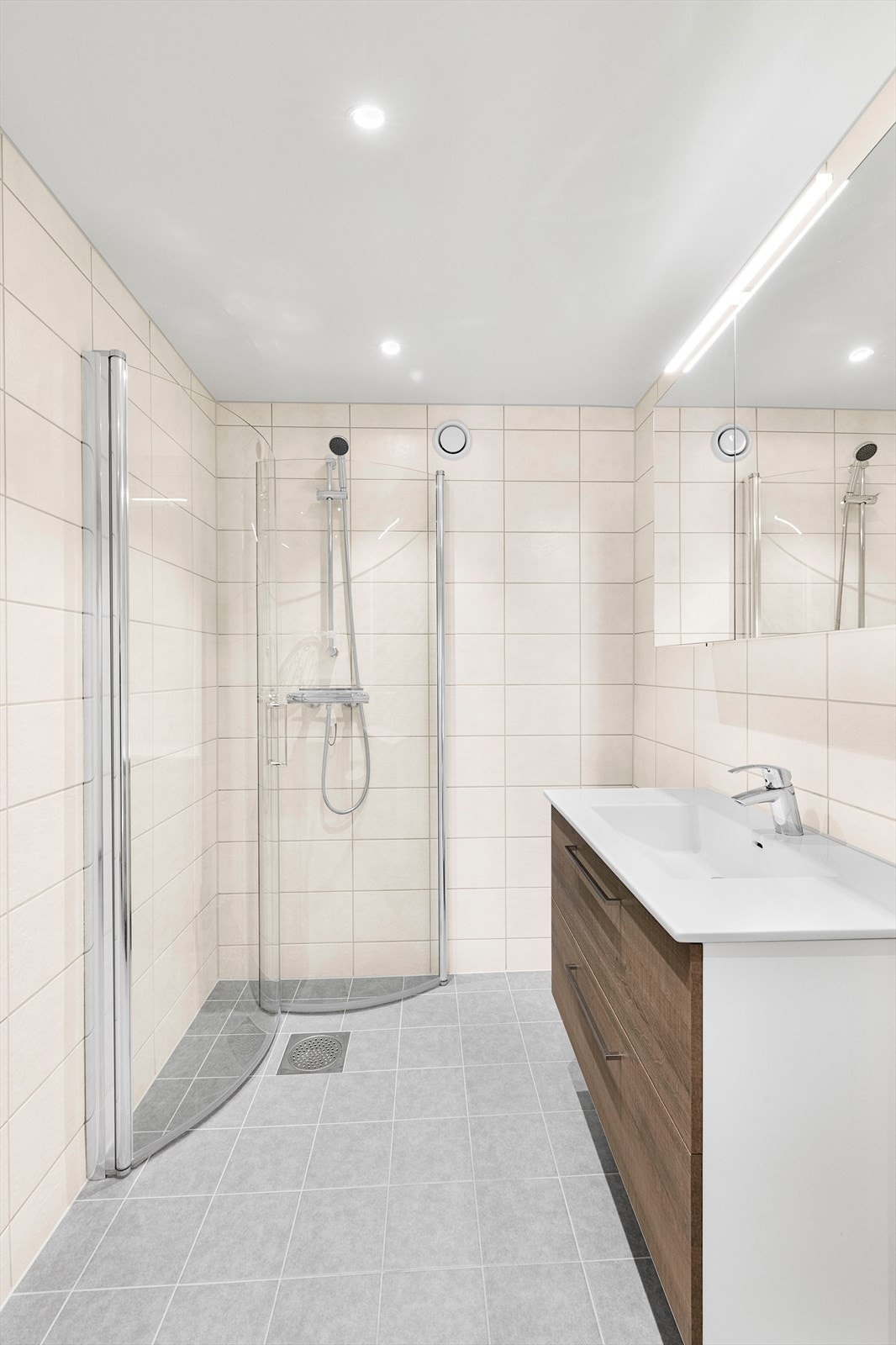 Badet har dusj på gulv med dører i herdet glass, og benkeskap med glatte fronter. Galleribilde