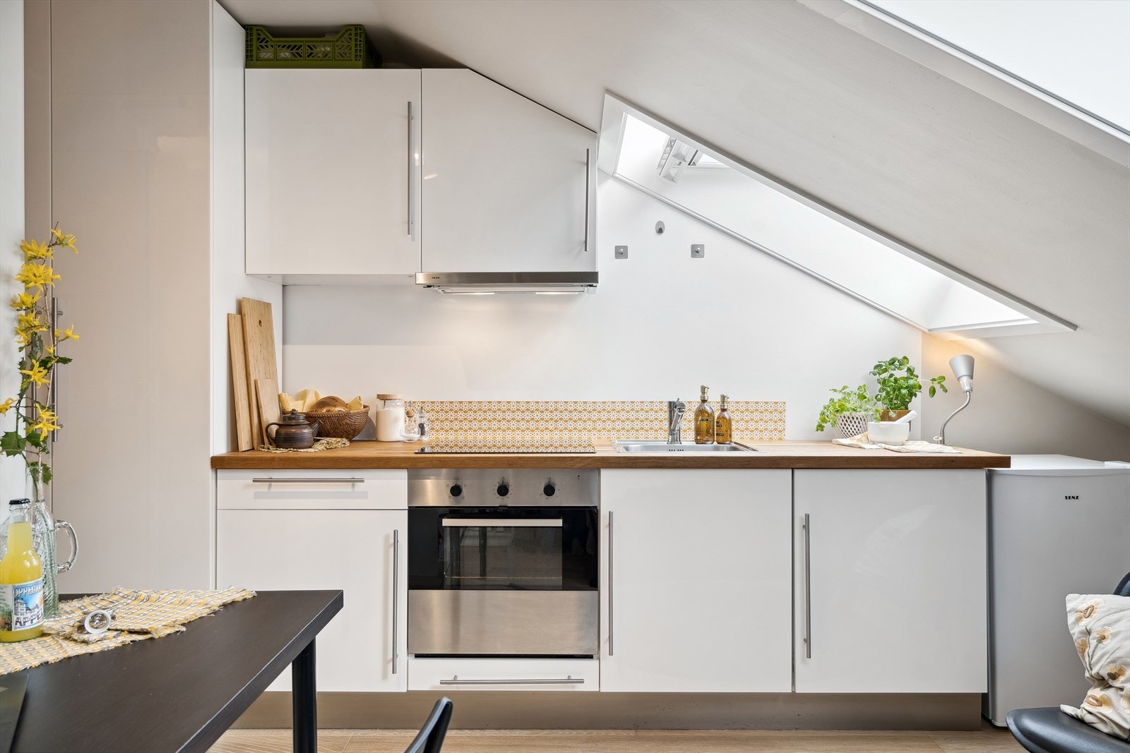 Pent kjøkken fra Ikea med høyglans fronter og benkeplate av tre. Kjøkkenet har integrert stekeovn/steketopp og kjøleskap. Galleribilde