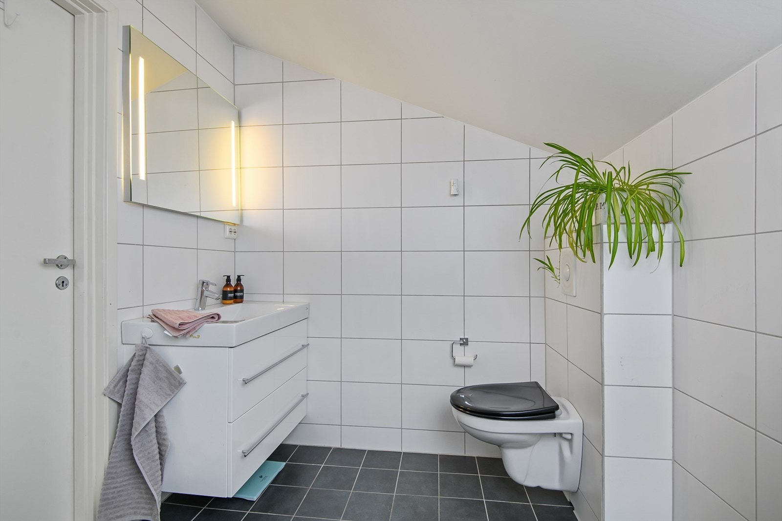 Flislagt bad med veggmontert toalett. Galleribilde