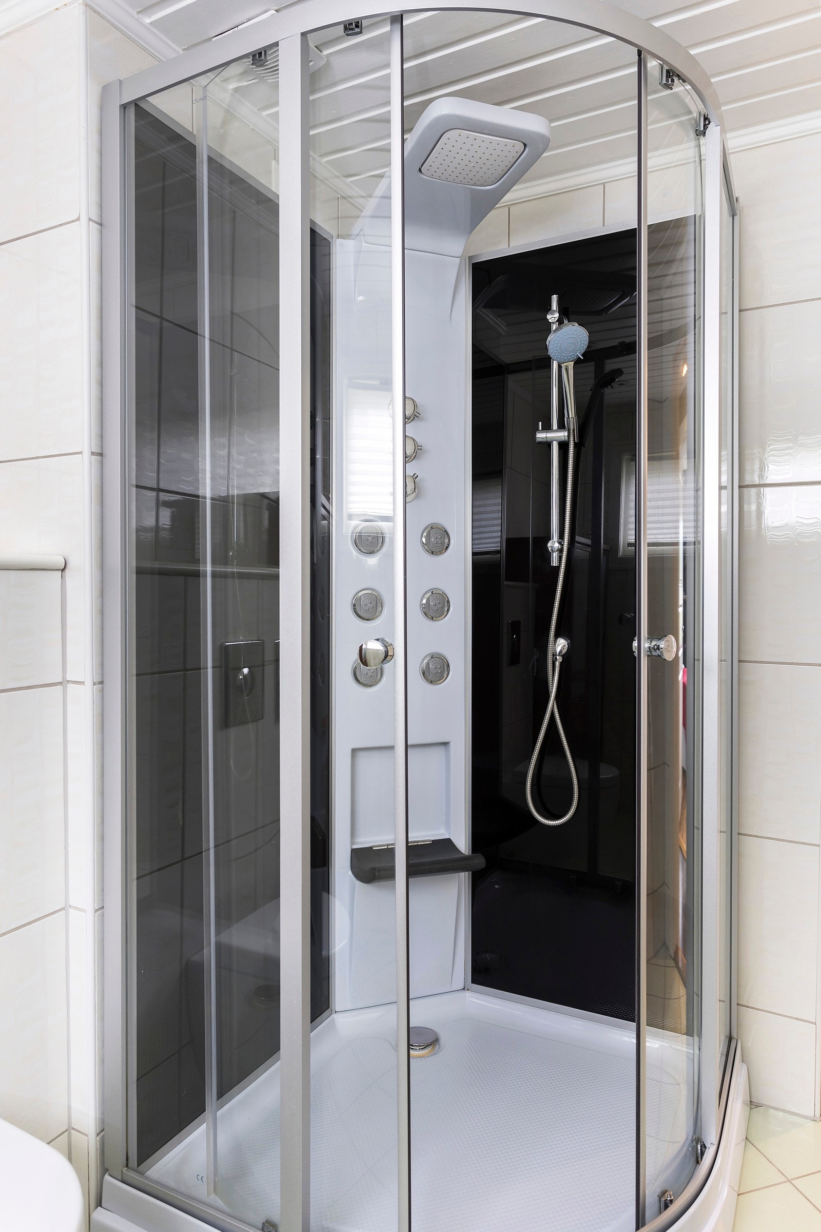 Innredningen på badet består av gulvstående servantinnredninger med ovenpåliggende servant med ett-greps armatur, speil og høyttaler på vegg over servanter, dusjkabinett og vegghengt toalett. Galleribilde