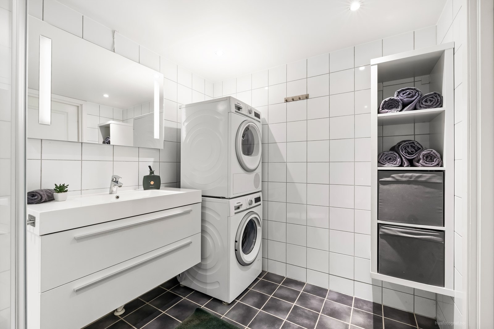 Tidløst bad med innredning og heldekkende servant, speil med integrert belysning, toalett, dusjkabinett og opplegg for vaskemaskin. Galleribilde