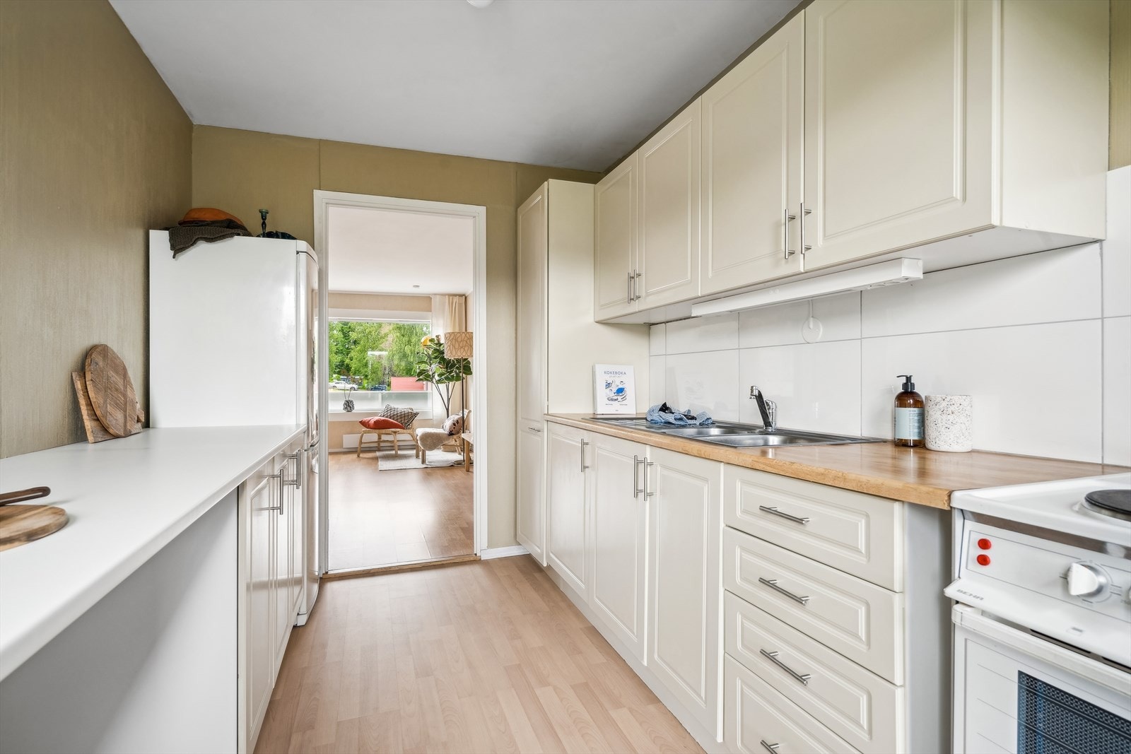 Kjøkkeninnredning er eldre, men velholdt med under -/overskap og profilerte fronter. Benkeplater av laminat med nedfelt kum i rustfritt stål og ettgreps blandebatteri. Frittstående hvitvarer. Galleribilde