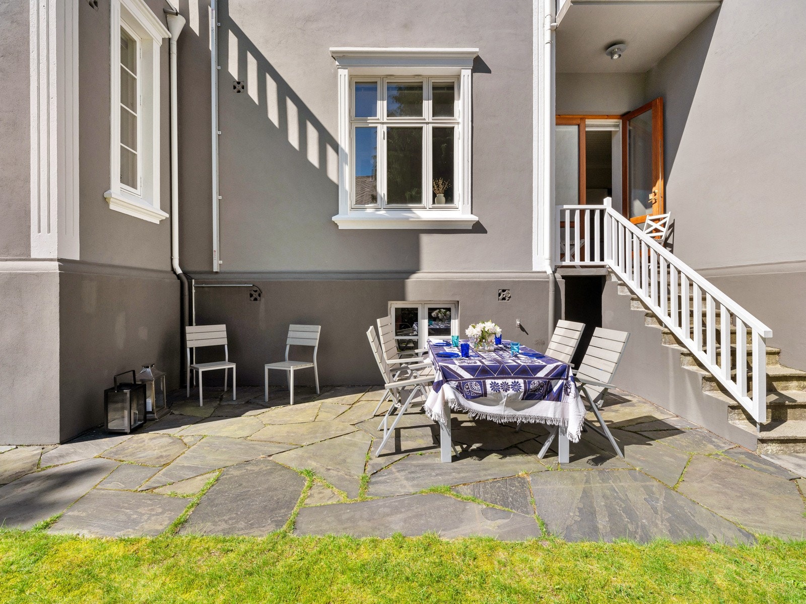 Fra kjøkkenet er det utgang til en liten balkong med støpt trapp og hvitmalt rekkverk ned til en markterrasse som ligger trukket inn mot husveggen. Galleribilde
