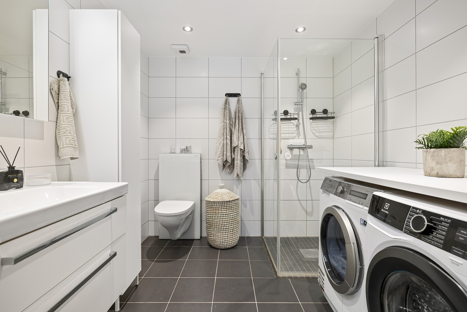 Badet er lekkert med vegghengt toalett og opplegg for vaskemaskin og tørketrommel. Her er det hvite veggfliser og sorte gulvfliser. Galleribilde