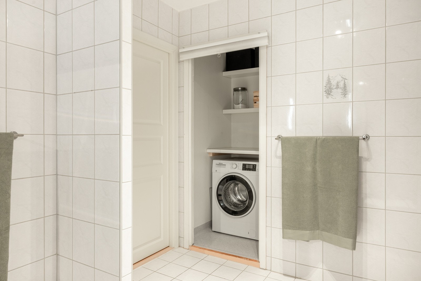 Praktisk vaskerom med inngang fra badet, opplegg til vaskemaskin, benkeplate og hyller for oppbevaring. Galleribilde