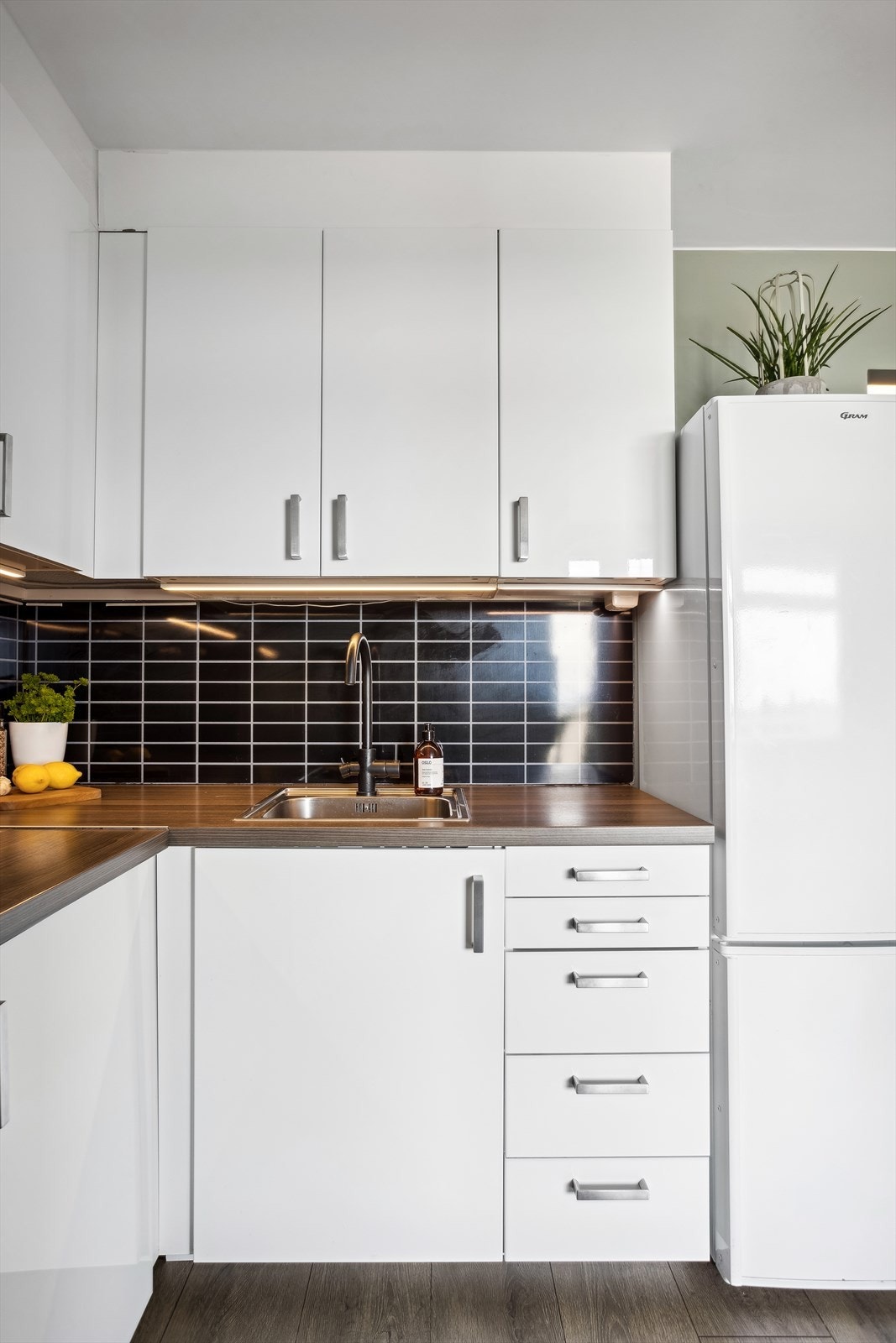 Kjøkkeninnredning med høyglansede folierte fronter, laminat benkeplate, laminatplater over benken, ventilator med stålhette og nedfelt stål benkebeslag. Galleribilde