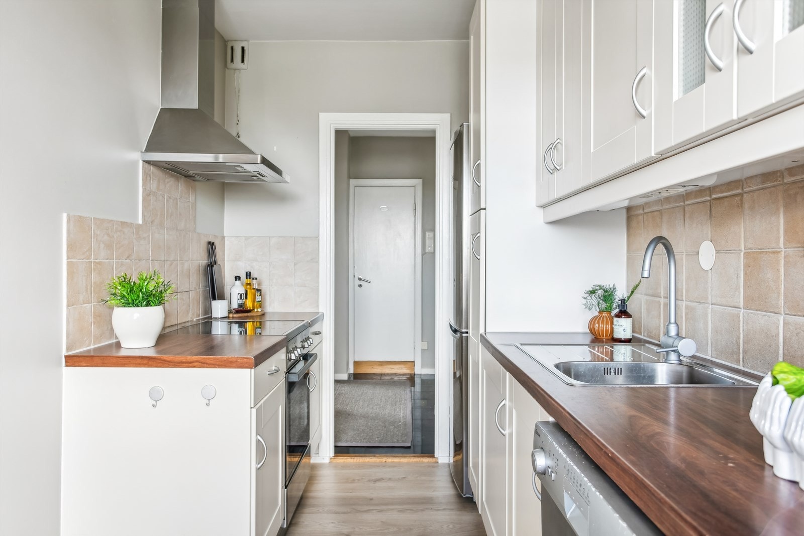 Kjøkkenet har en tidløs innredning med hvite profilerte fronter, enkelte overskap med glassfelt, laminat benkeplate med nedfelt kjøkkenvask og fliser på vegg over kjøkkenbenk Galleribilde
