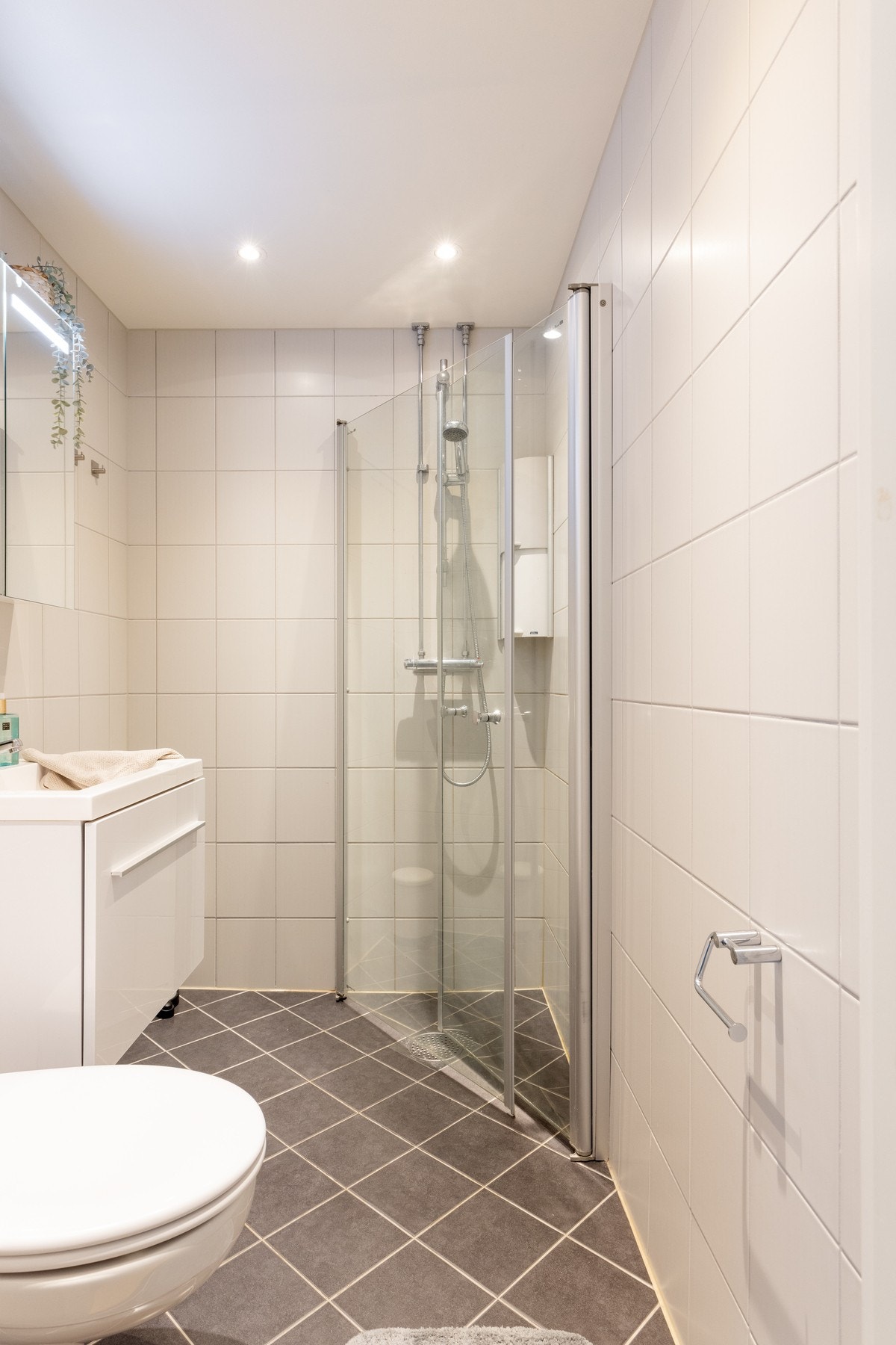 Badet har en stilren innredning med servant, speilskap med belysning, dusjhjørne med innfellbare glassdører og et vegghengt toalett. Galleribilde