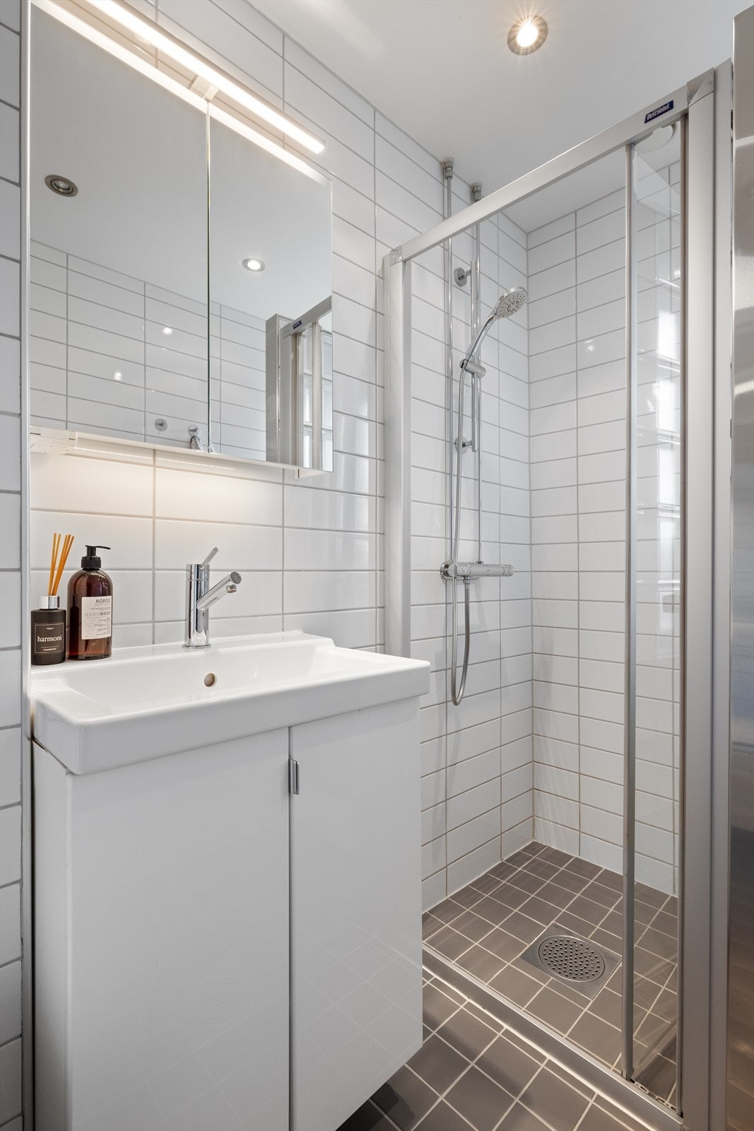 Badet inneholder baderomsinnredning med skap, overlimt servant og speilskap med belysning, veggmontert toalett samt dusjhjørne Galleribilde