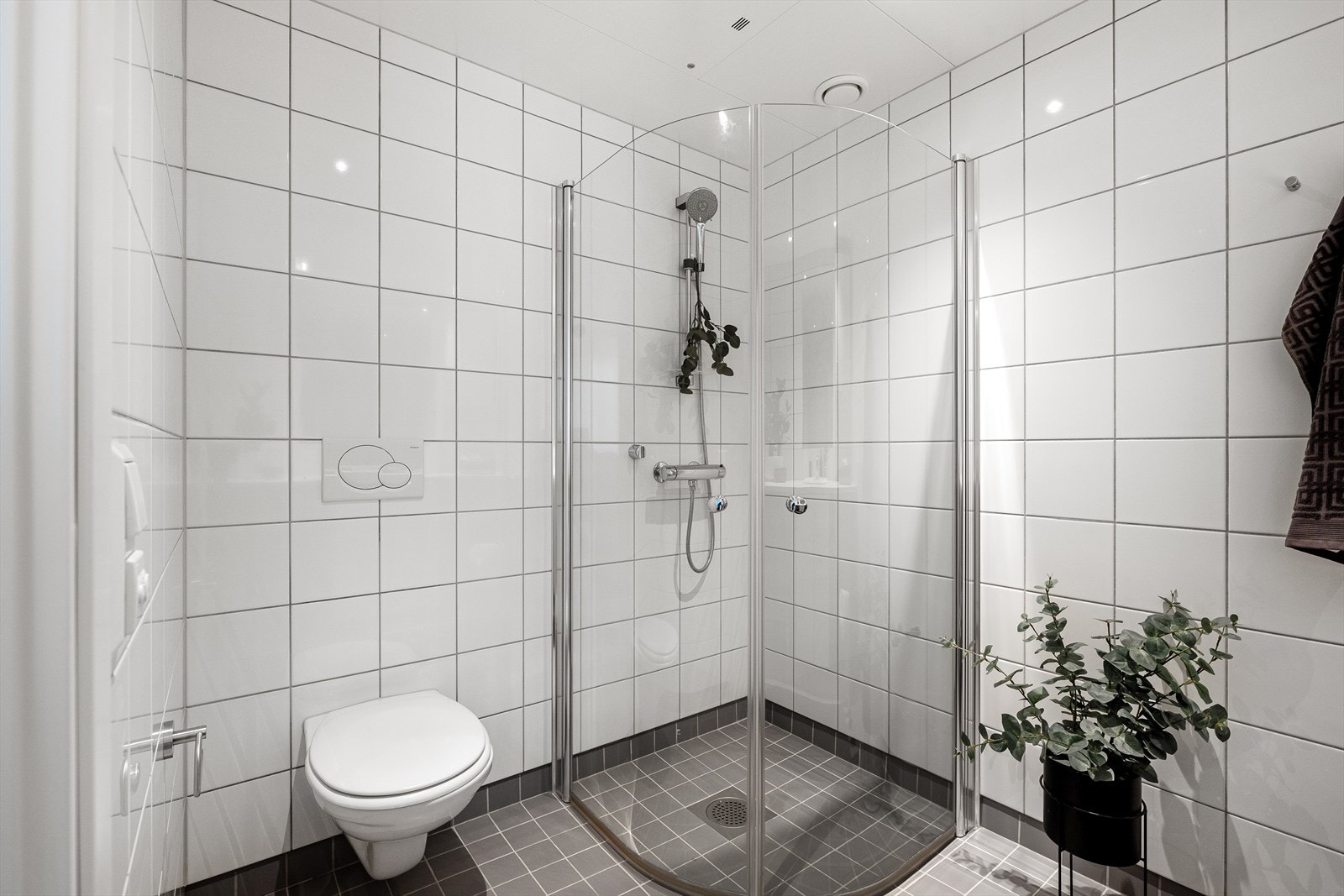 Videre er det ett vegghengt skap, vegghengt toalett med innebygget sisterne og dusjvegger/hjørne. Galleribilde