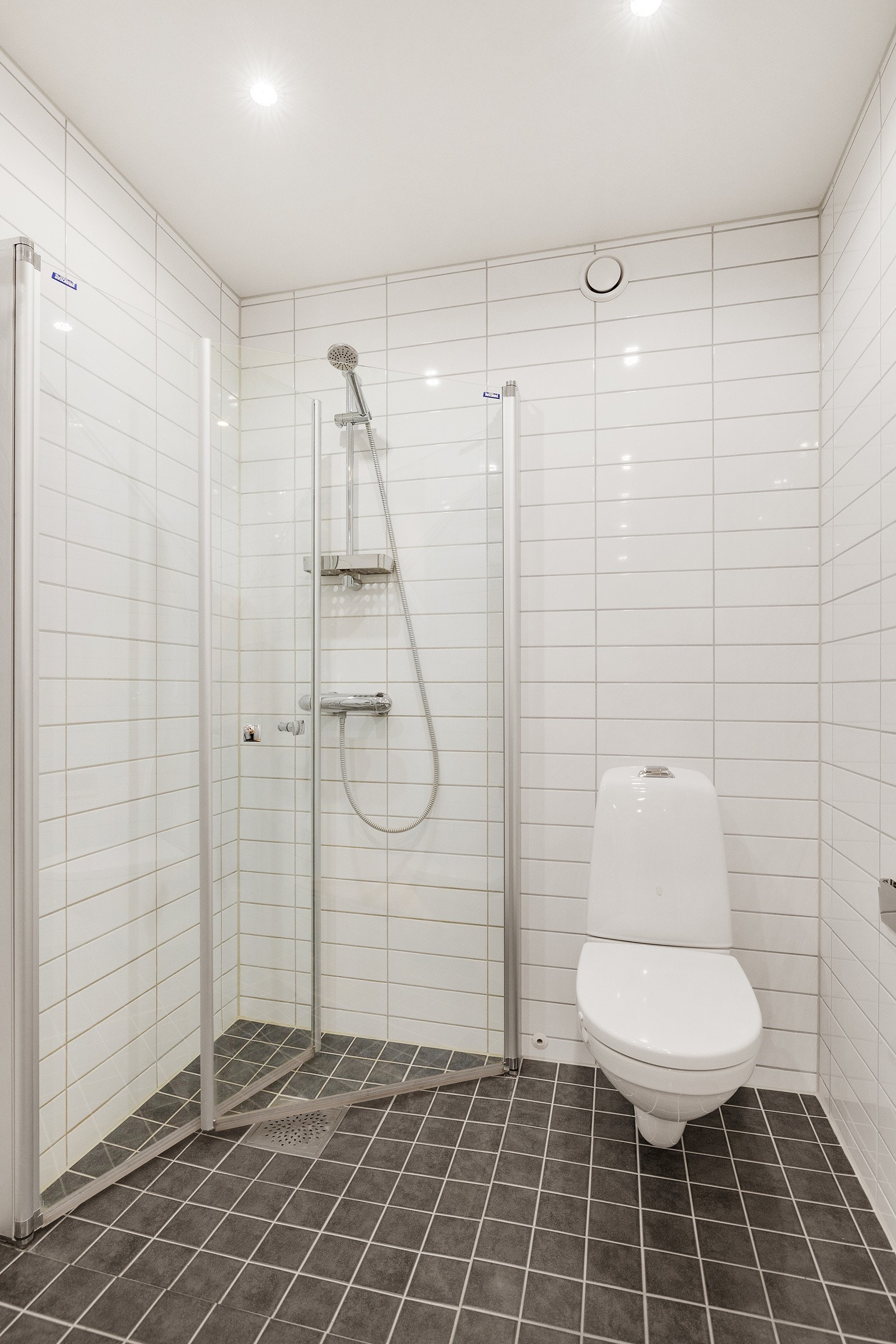 Et lyst og lekkert bad med eget dusjhjørne, vegghengt toalett og servant med over -og underskap. Galleribilde