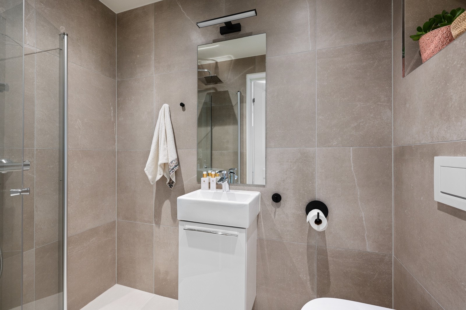 Det andre badet i 2. etasje er også lekkert og moderne med flislagte flater, dusjhjørne, vegghengt wc og innredning med toppmontert servant og etthånds blandebatteri. Galleribilde