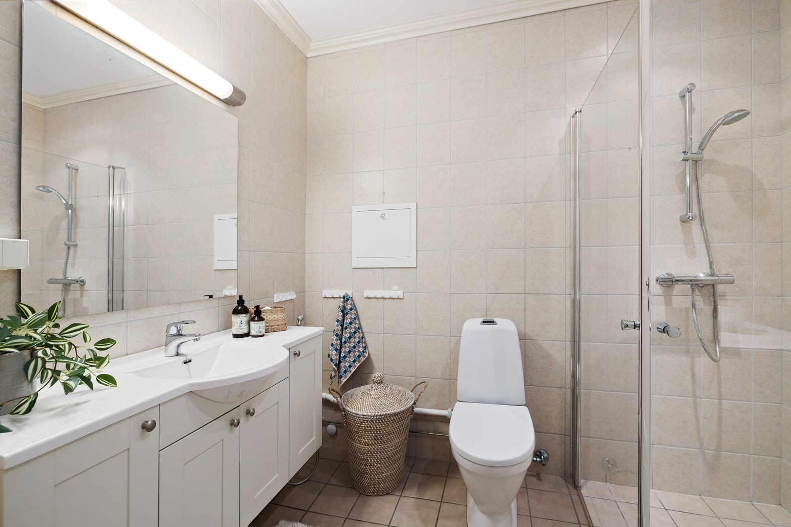 Badet har overflater med beige fliser, samt gulvvarme og opplegg for vaskemaskin. Galleribilde