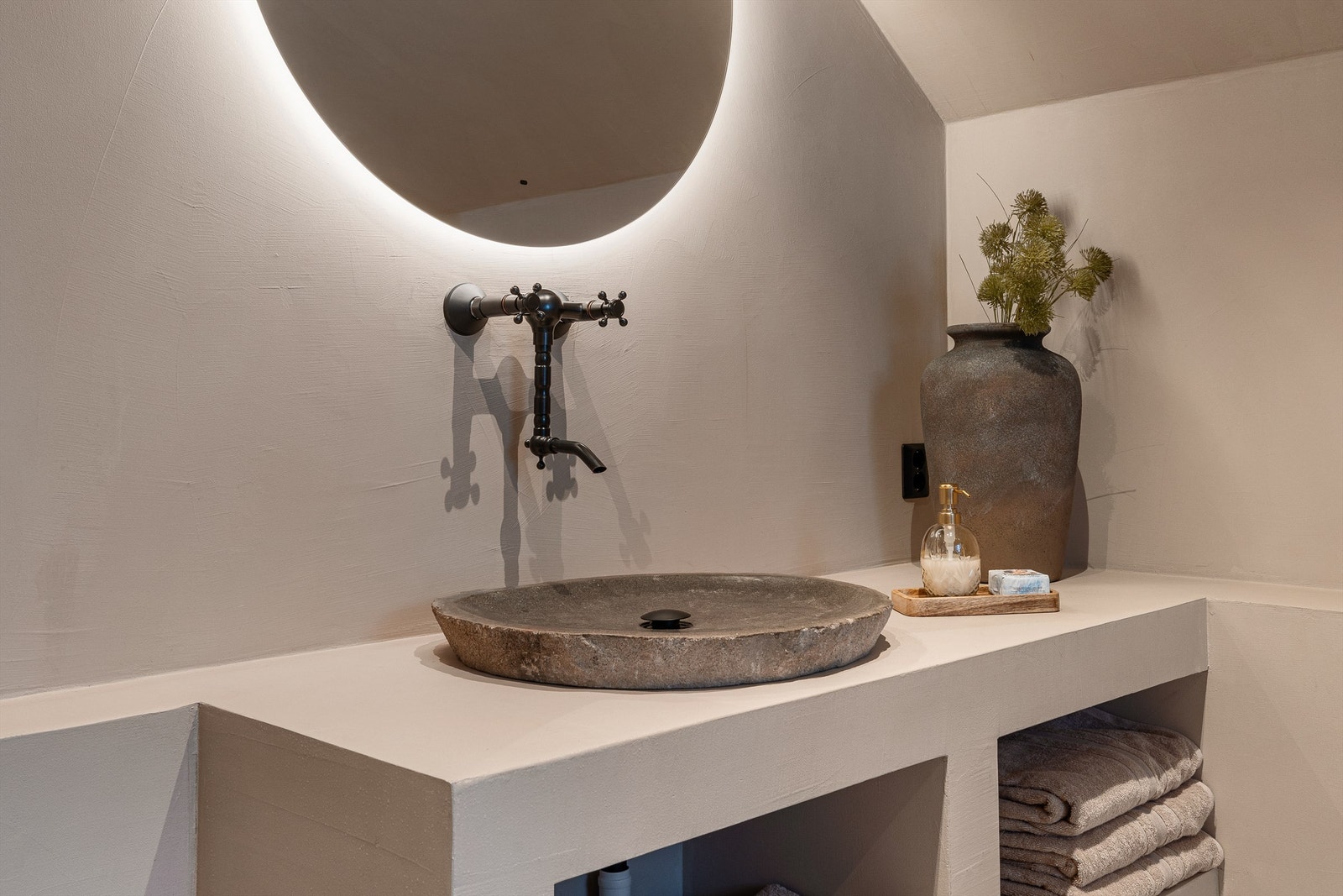 Servantbenk med hyller er laget av microsement. Servant i stein og et rundt speil med integrert belysning bidrar til en fin miks av det moderne og rustikke. Galleribilde