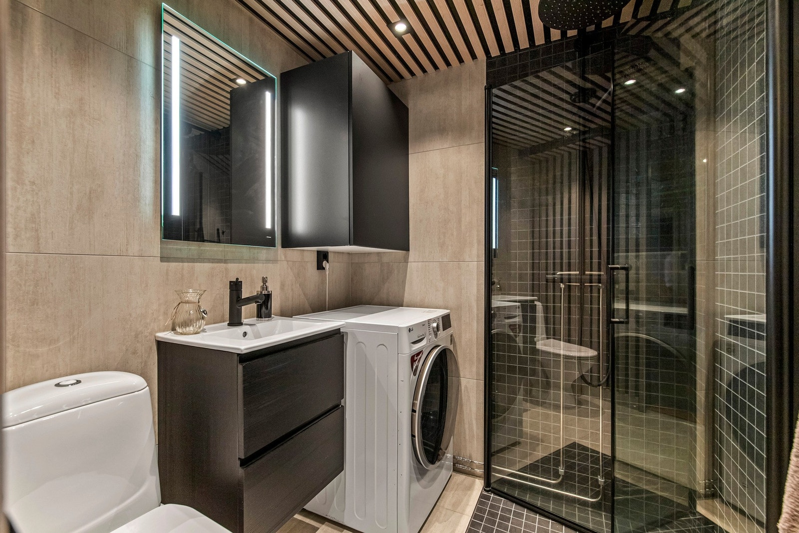 Innredet med servantinnredning, dusjdører, opplegg for vaskemaskin og wc. Galleribilde