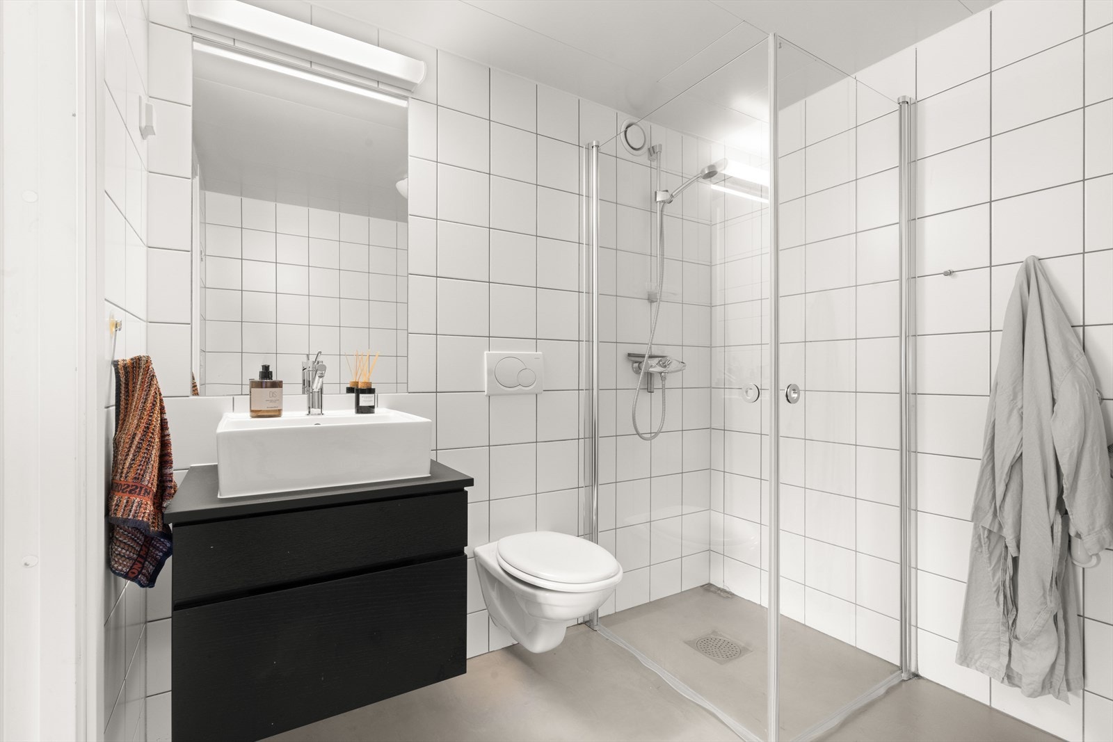 Innredningen består av et praktisk servantskap med en stilren, påliggende servant og 1-greps blandebatteri, dusjhjørnet med svingbare glassdører som gir en romslig følelse, og et vegghengt toalettet. Galleribilde