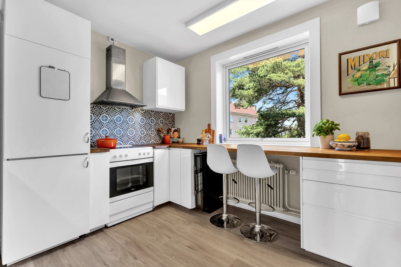 Kjøkkeninnredning med fronter i høyglanset utførelse, enkelte glassfronter i overskap, belysning under overskap og fliser på vegg over benkeskap. Galleribilde