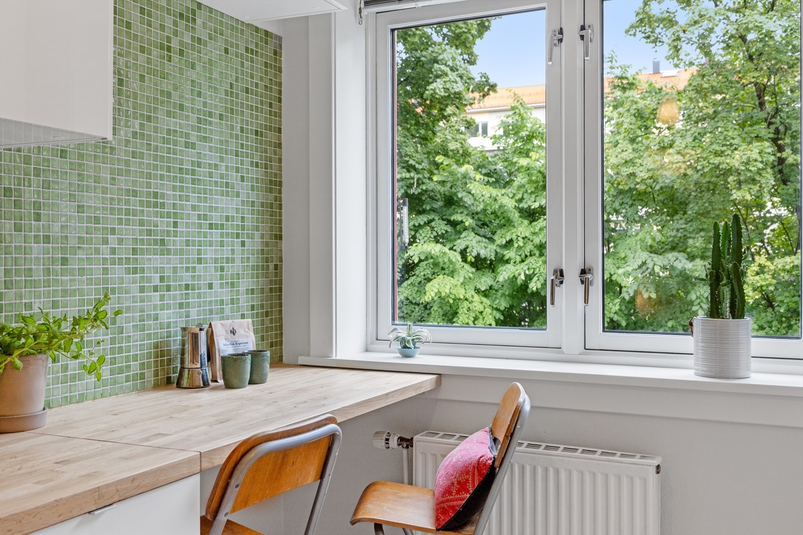 Lyst og moderne kjøkken med IKEA innredning, nyslipt heltre benkeplate og kule mosaikkfliser. Spiseplass ved vinduet og grønt utsyn. Galleribilde