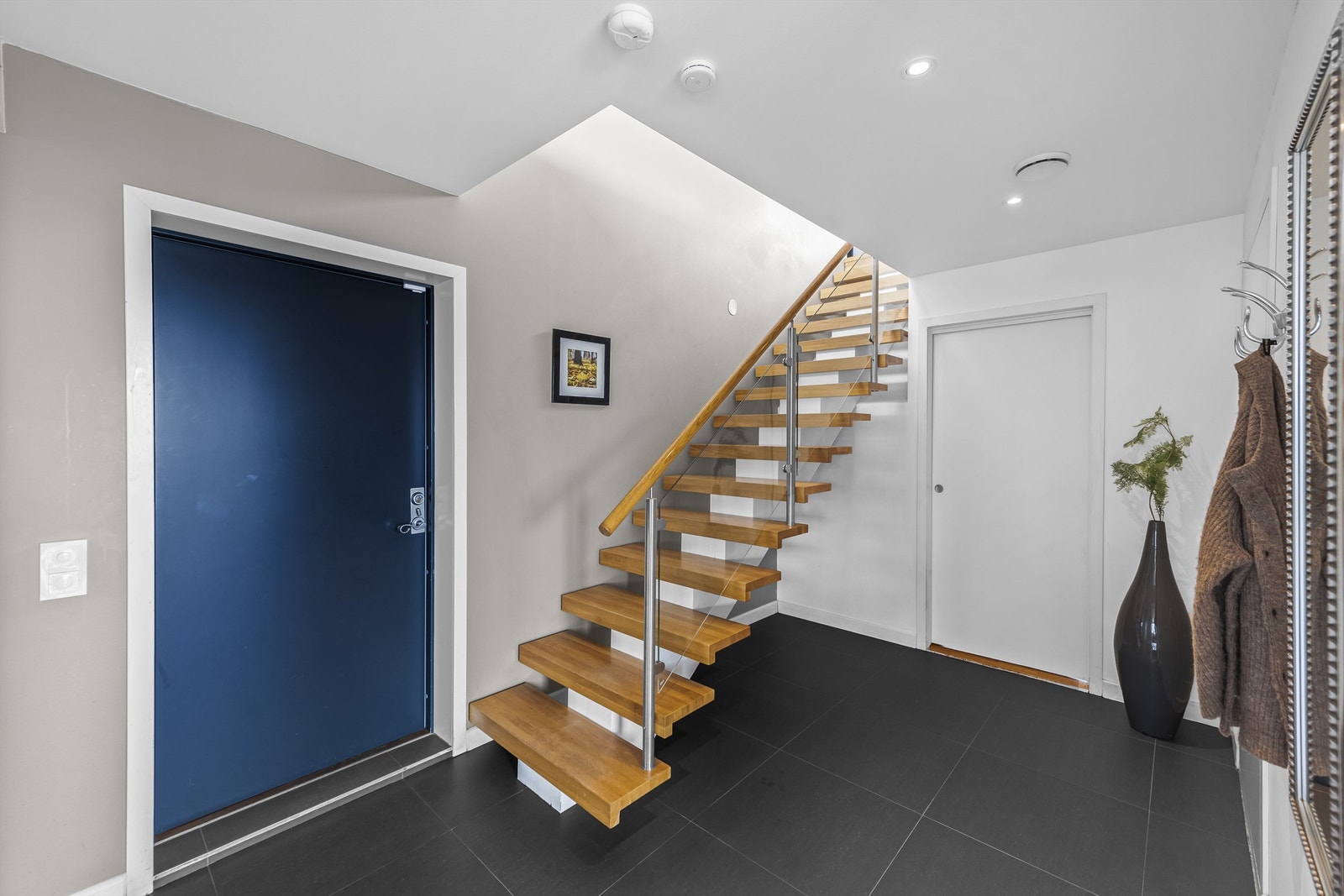 Boligen har også inngang fra første etasje, til en flislagt gang med åpen løsning til kjøkken og hovedstue. Gangen har downlight, lysmalte vegger, listefritt tak med downlight og åpen garderobeløsning. Galleribilde