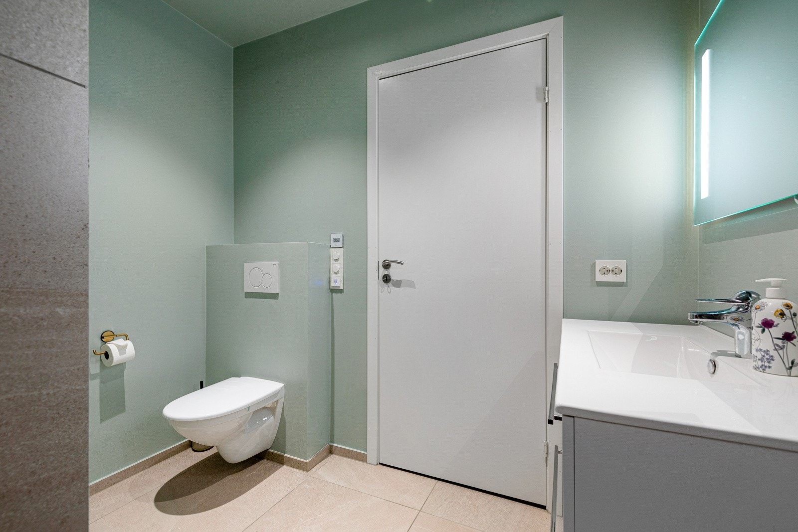 Badet ved inngangen inneheld veggmontert klosett, dusjnisje med blandebatteri og dusj, heilstøypt vask i kvit enkel foliert innredning og med veggmonert speigel med innfelt belysning. Galleribilde